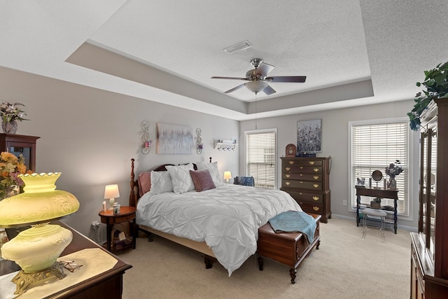 carpeted bedroom with a raised ceiling, ceiling fan, and multiple windows