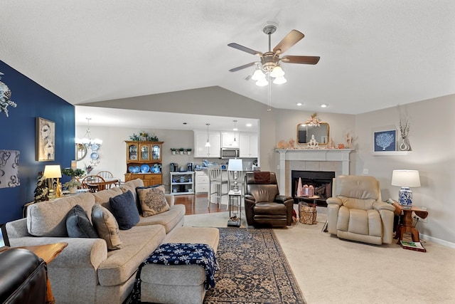 carpeted living room with ceiling fan with notable chandelier, a tile fireplace, a textured ceiling, and vaulted ceiling