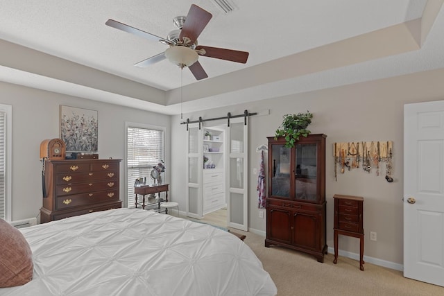 bedroom with ceiling fan, light carpet, a barn door, and a tray ceiling