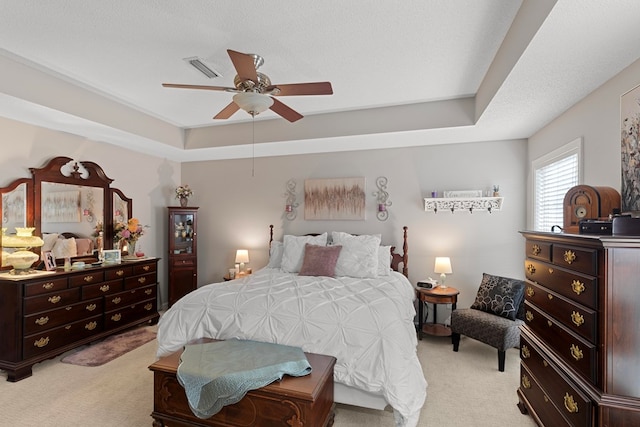 bedroom with a textured ceiling, light carpet, ceiling fan, and a tray ceiling