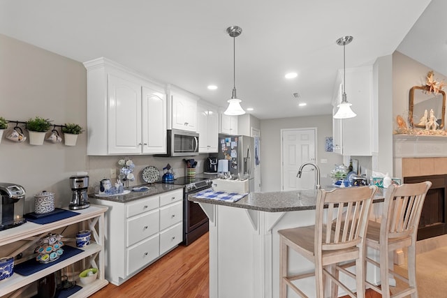 kitchen with appliances with stainless steel finishes, hanging light fixtures, dark stone counters, white cabinets, and light hardwood / wood-style flooring