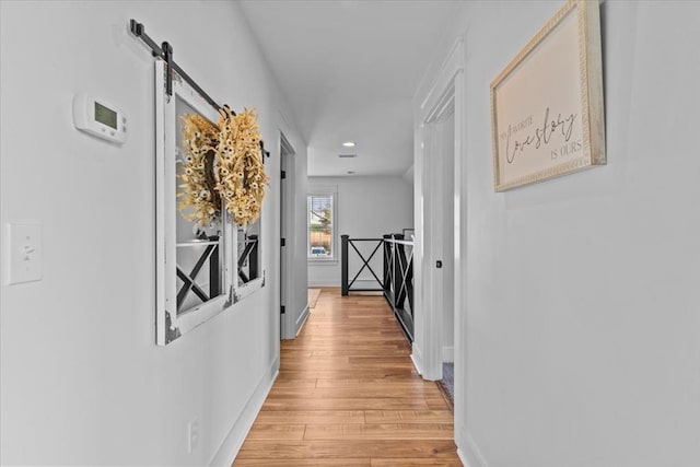 hall with a barn door and light hardwood / wood-style floors