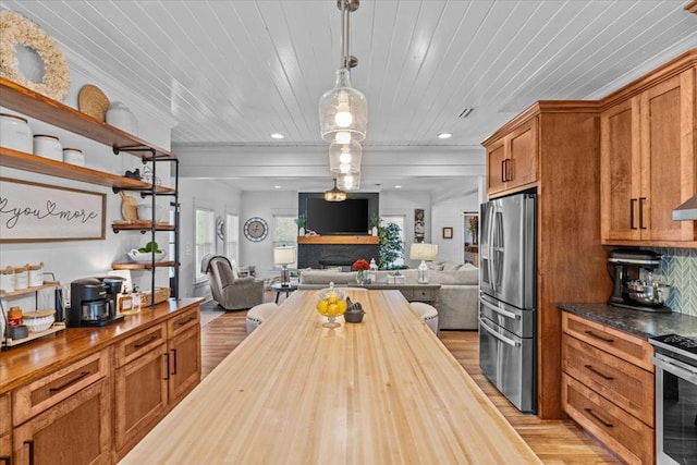 kitchen with appliances with stainless steel finishes, butcher block countertops, decorative light fixtures, decorative backsplash, and light hardwood / wood-style floors