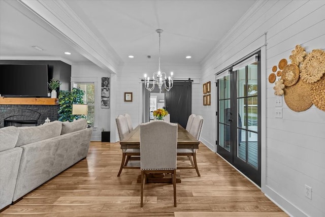 dining space with a brick fireplace, a notable chandelier, light hardwood / wood-style flooring, and ornamental molding