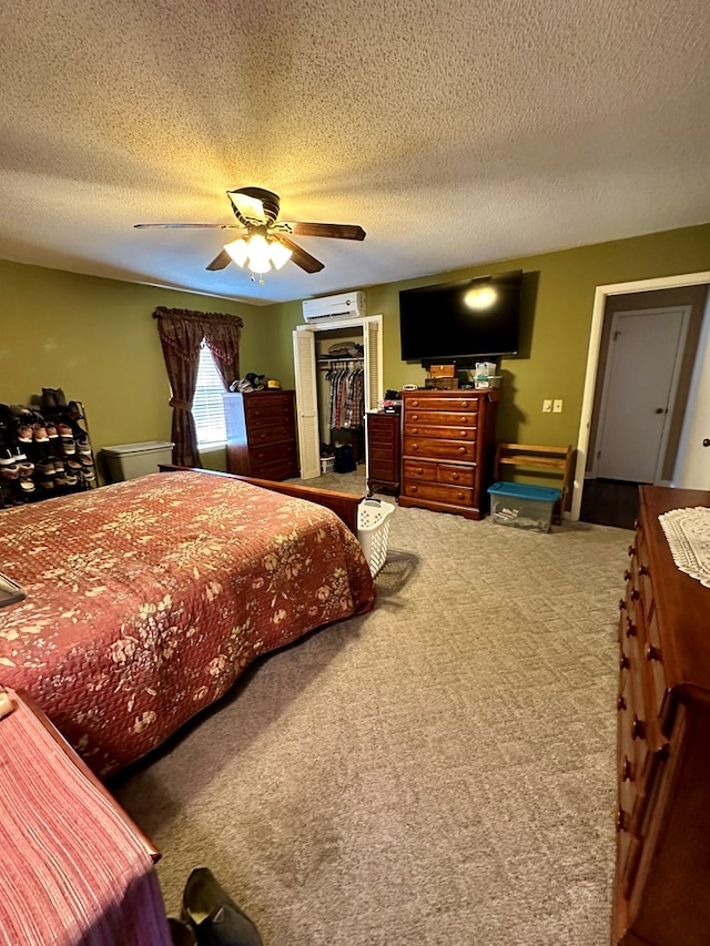 carpeted bedroom featuring a textured ceiling, a spacious closet, a closet, ceiling fan, and a wall mounted air conditioner