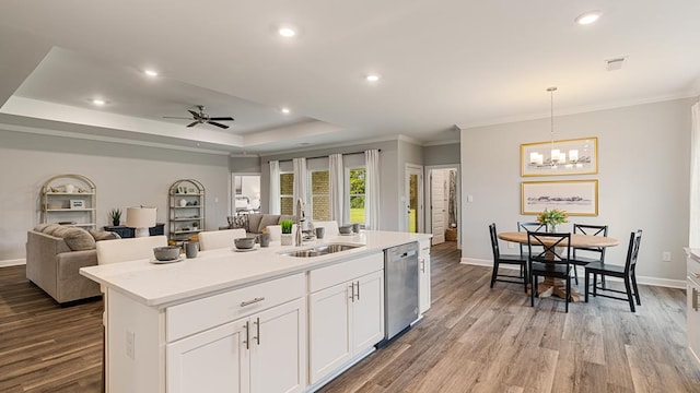 kitchen with stainless steel dishwasher, a tray ceiling, a kitchen island with sink, sink, and white cabinetry