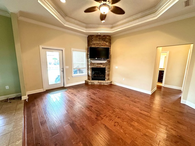 unfurnished living room featuring hardwood / wood-style floors, a fireplace, ornamental molding, ceiling fan, and a tray ceiling