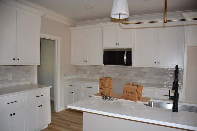 110 Mikala Ct, Enterprise, AL 36330 - kitchen featuring stainless steel microwave, white cabinets, backsplash, light wood-style floors, and ornamental molding