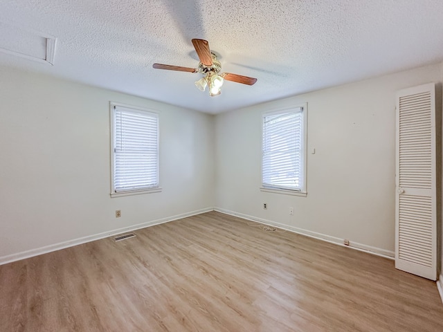 empty room featuring a textured ceiling, light wood-type flooring, plenty of natural light, and baseboards