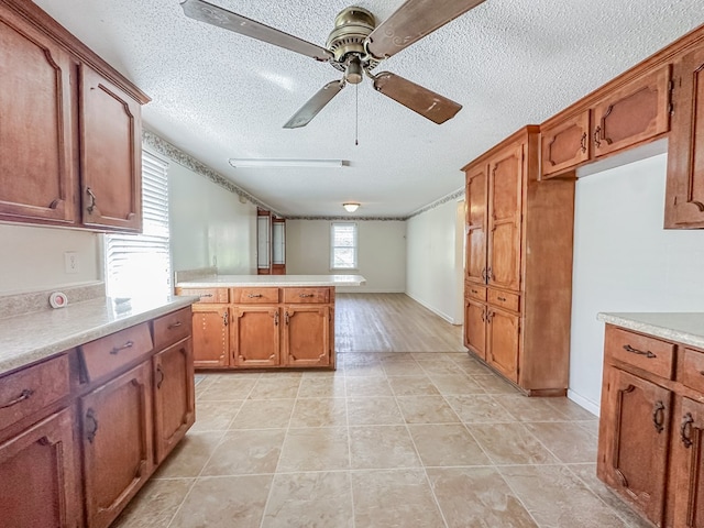 kitchen with ceiling fan, brown cabinets, a peninsula, light countertops, and a textured ceiling