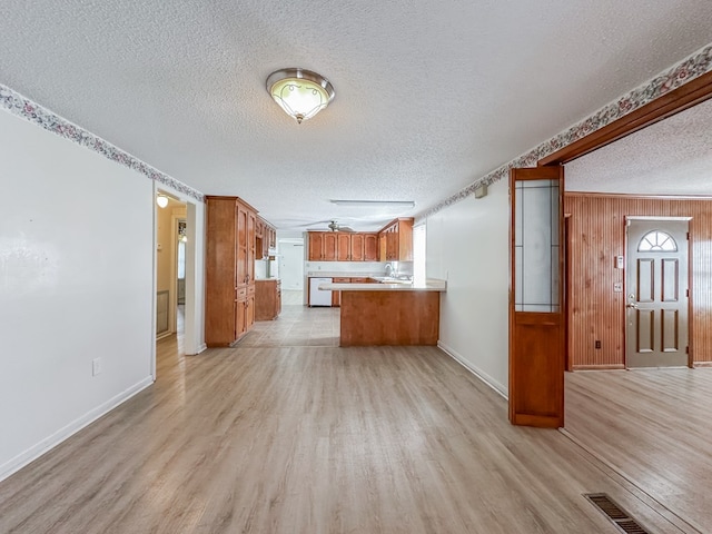 unfurnished living room featuring a textured ceiling, wood walls, visible vents, baseboards, and light wood-type flooring