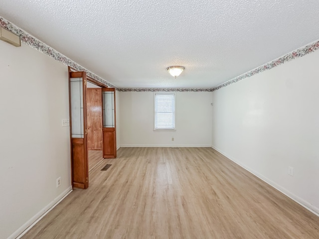 empty room featuring light wood-style floors, visible vents, a textured ceiling, and baseboards