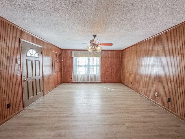 unfurnished room featuring light wood finished floors, wood walls, and crown molding