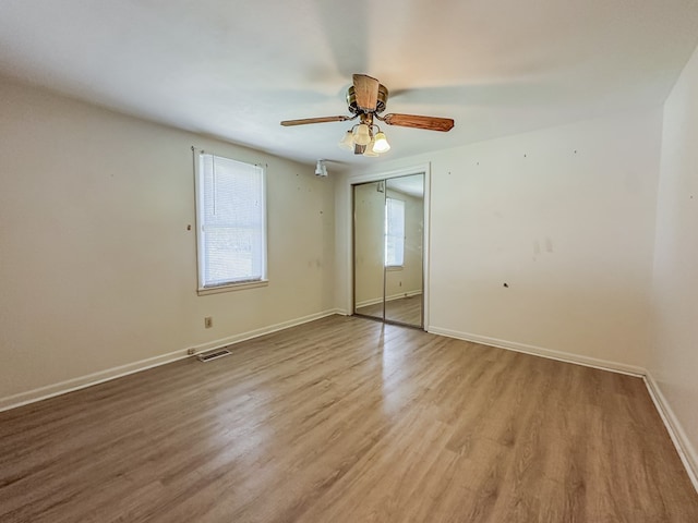 unfurnished bedroom with wood finished floors, a ceiling fan, visible vents, baseboards, and a closet