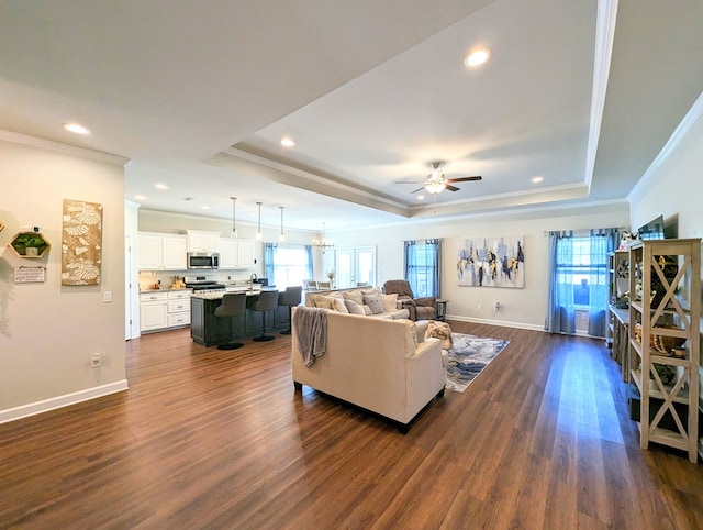 living room with a tray ceiling, ceiling fan, dark wood-type flooring, and a healthy amount of sunlight