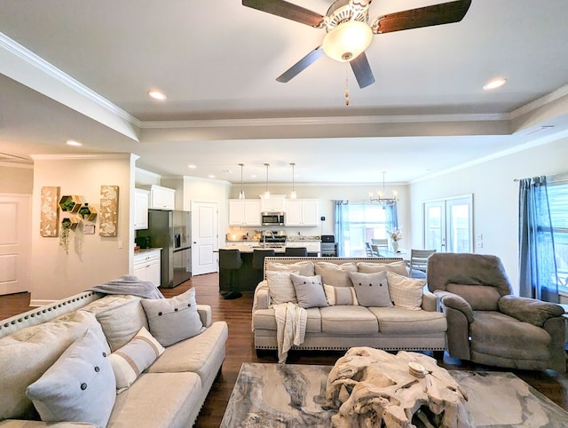 living room with dark wood-type flooring, ceiling fan with notable chandelier, and ornamental molding