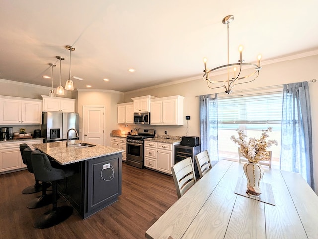 kitchen featuring a kitchen island with sink, white cabinets, hanging light fixtures, light stone countertops, and stainless steel appliances