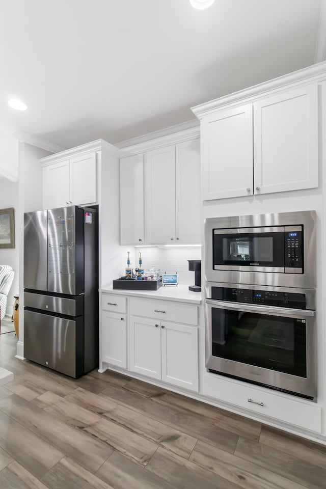 kitchen with light wood-type flooring, ornamental molding, white cabinets, and appliances with stainless steel finishes