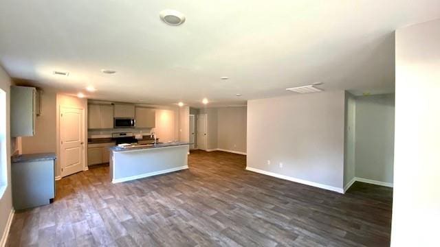 kitchen featuring a center island with sink, sink, white stove, and dark wood-type flooring