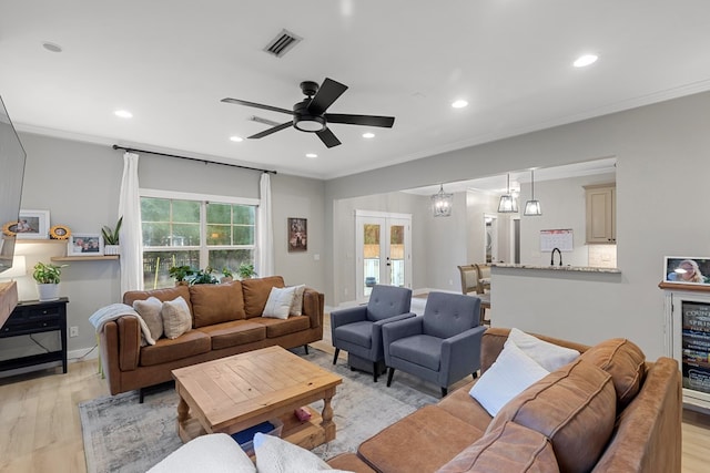 living room with ornamental molding, light wood-type flooring, french doors, and ceiling fan with notable chandelier