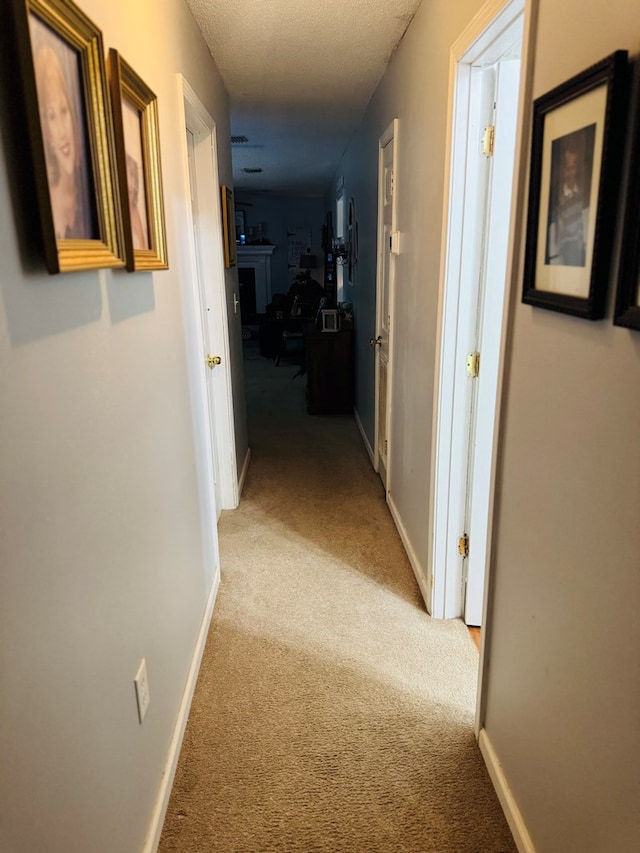 corridor featuring a textured ceiling, light carpet, and baseboards