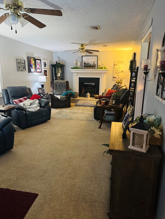 living area with a textured ceiling, visible vents, ceiling fan, carpet floors, and a glass covered fireplace