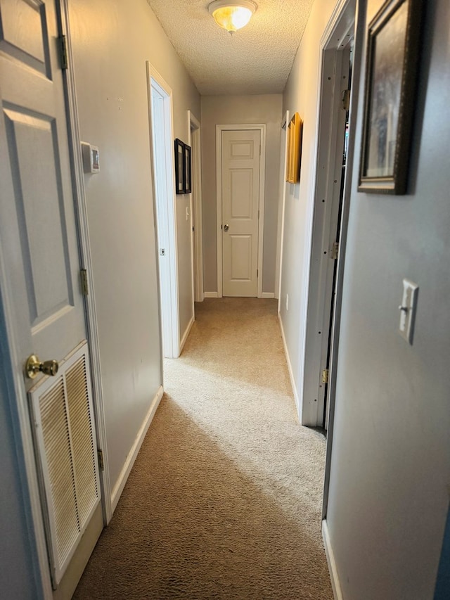 hallway with a textured ceiling, visible vents, baseboards, and light carpet