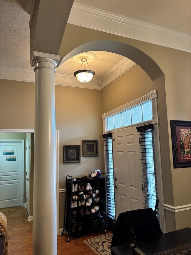 entryway with crown molding, hardwood / wood-style floors, a textured ceiling, and ornate columns