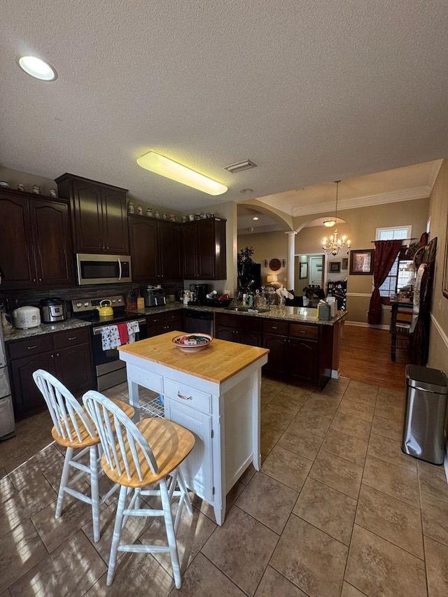 kitchen with butcher block counters, dark brown cabinets, appliances with stainless steel finishes, a kitchen island, and pendant lighting