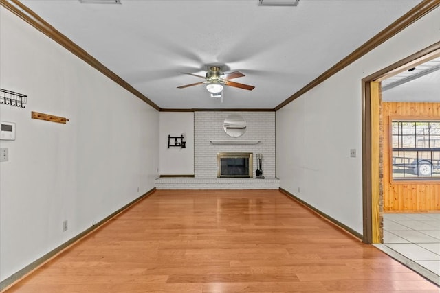 unfurnished living room featuring crown molding, ceiling fan, light wood-type flooring, and a brick fireplace