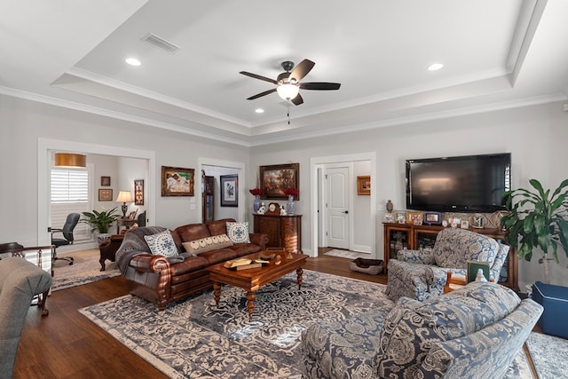 living room featuring dark hardwood / wood-style flooring, ceiling fan, a tray ceiling, and ornamental molding