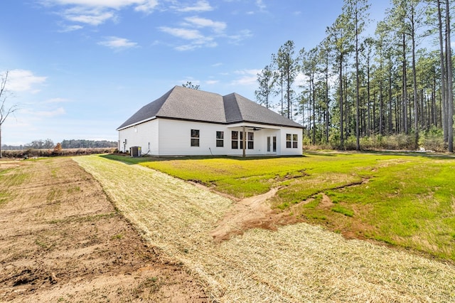 view of side of property with a shingled roof, central AC, and a yard