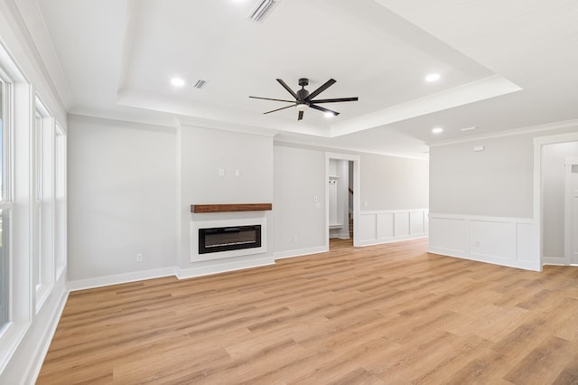 unfurnished living room with a glass covered fireplace, a raised ceiling, visible vents, and light wood finished floors