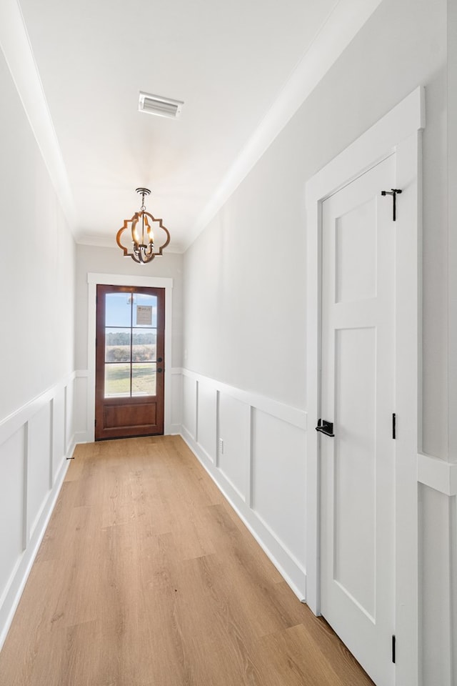 doorway to outside featuring light wood-type flooring, visible vents, a decorative wall, and an inviting chandelier