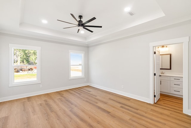 unfurnished bedroom featuring a raised ceiling, multiple windows, and light wood finished floors