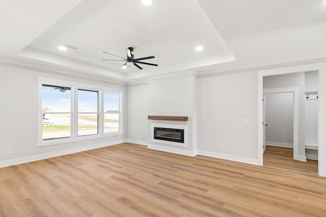 unfurnished living room with ceiling fan, baseboards, a raised ceiling, light wood finished floors, and a glass covered fireplace