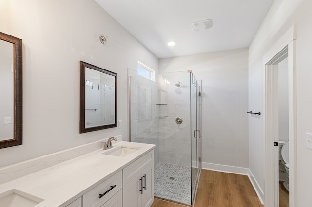 bathroom featuring toilet, wood finished floors, a sink, a shower stall, and double vanity