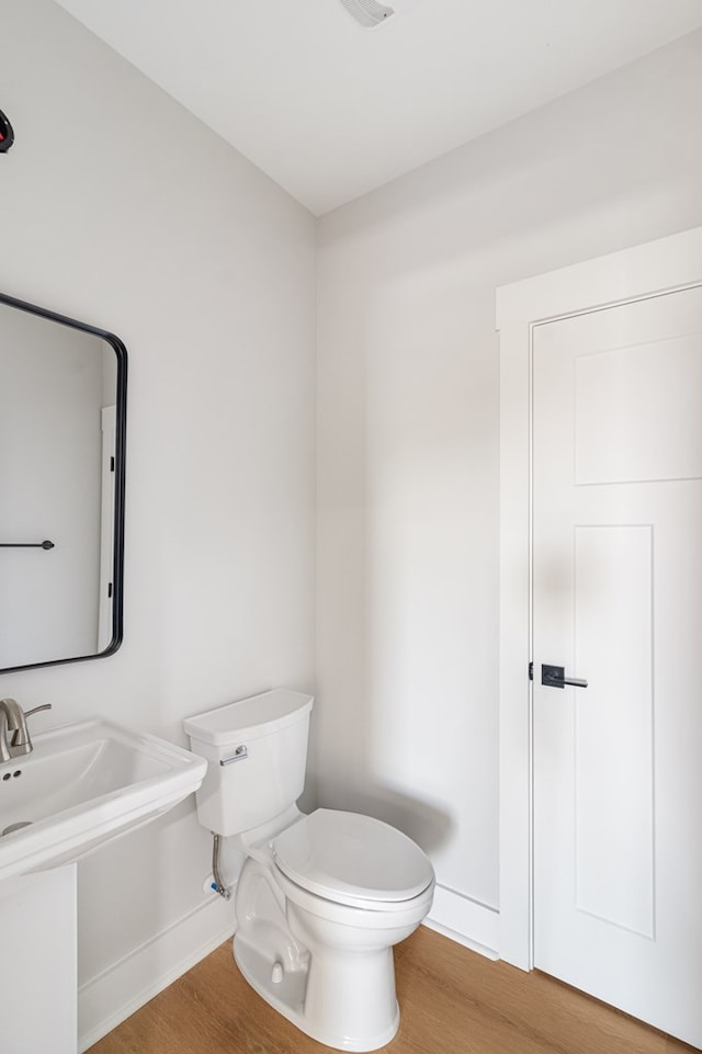 half bath with baseboards, toilet, and wood finished floors