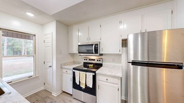 kitchen with appliances with stainless steel finishes, white cabinetry, light stone counters, light hardwood / wood-style floors, and a textured ceiling