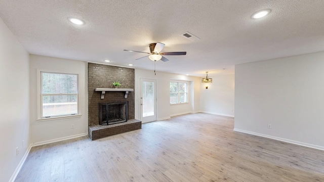 unfurnished living room with ceiling fan, light hardwood / wood-style floors, a brick fireplace, and a textured ceiling