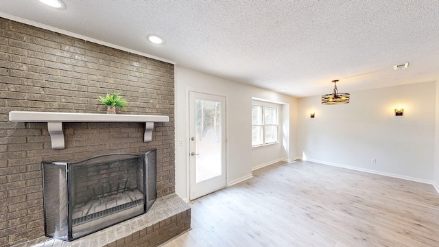 unfurnished living room with a brick fireplace, light hardwood / wood-style flooring, and a textured ceiling