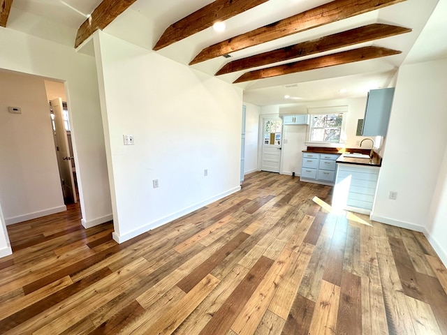 unfurnished living room featuring beamed ceiling, light wood-type flooring, and sink