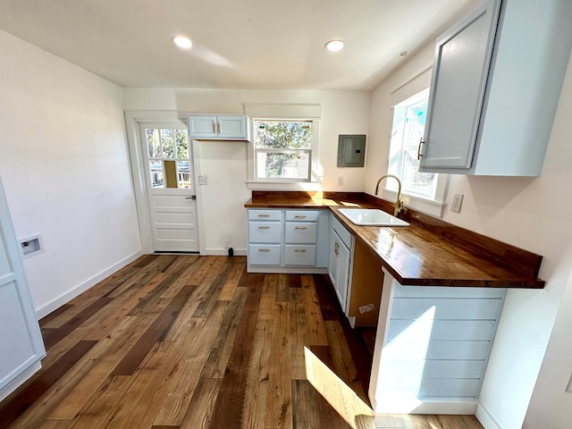 kitchen featuring sink, butcher block countertops, electric panel, white cabinetry, and dark hardwood / wood-style floors