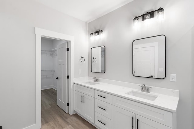 full bath featuring double vanity, a spacious closet, wood finished floors, and a sink