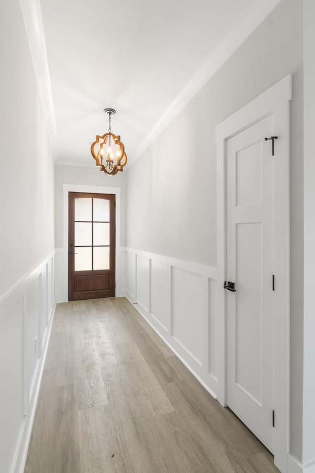 interior space with a wainscoted wall, a decorative wall, light wood finished floors, and an inviting chandelier