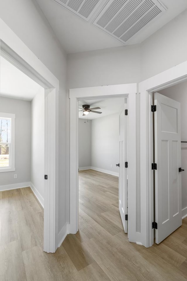 hall with light wood-type flooring, visible vents, and baseboards