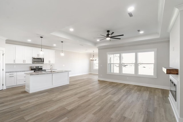 kitchen with appliances with stainless steel finishes, a tray ceiling, open floor plan, and white cabinets