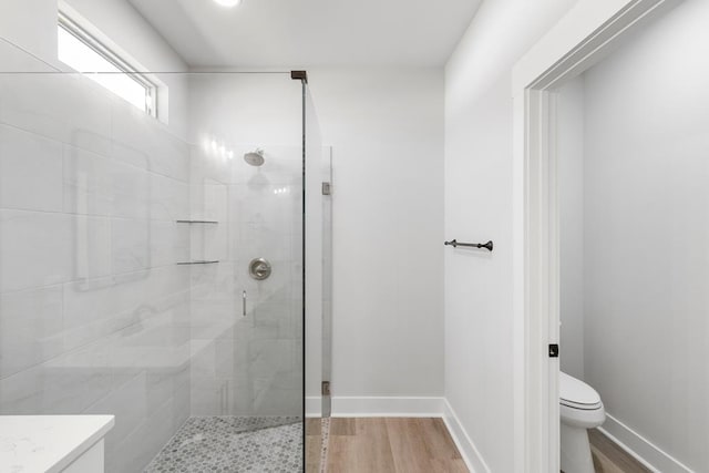 bathroom with toilet, a stall shower, vanity, wood finished floors, and baseboards