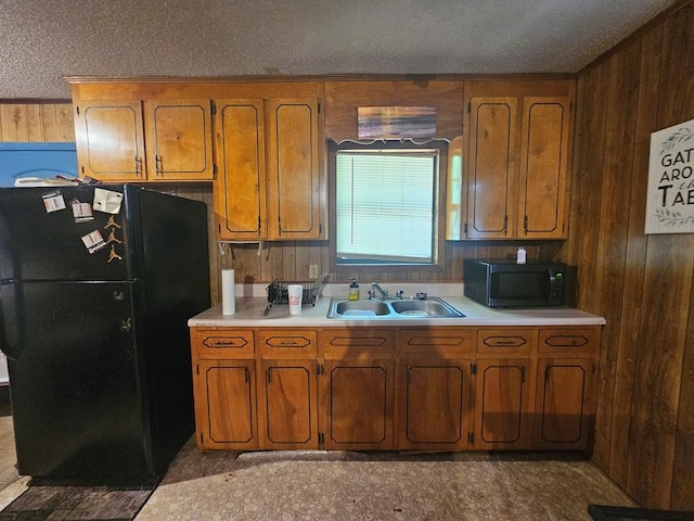 kitchen with a textured ceiling, wood walls, black appliances, and sink