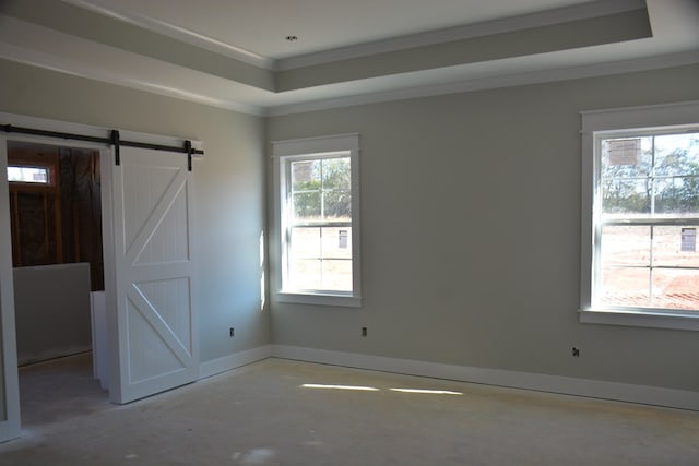 empty room with a barn door, a healthy amount of sunlight, ornamental molding, and a tray ceiling